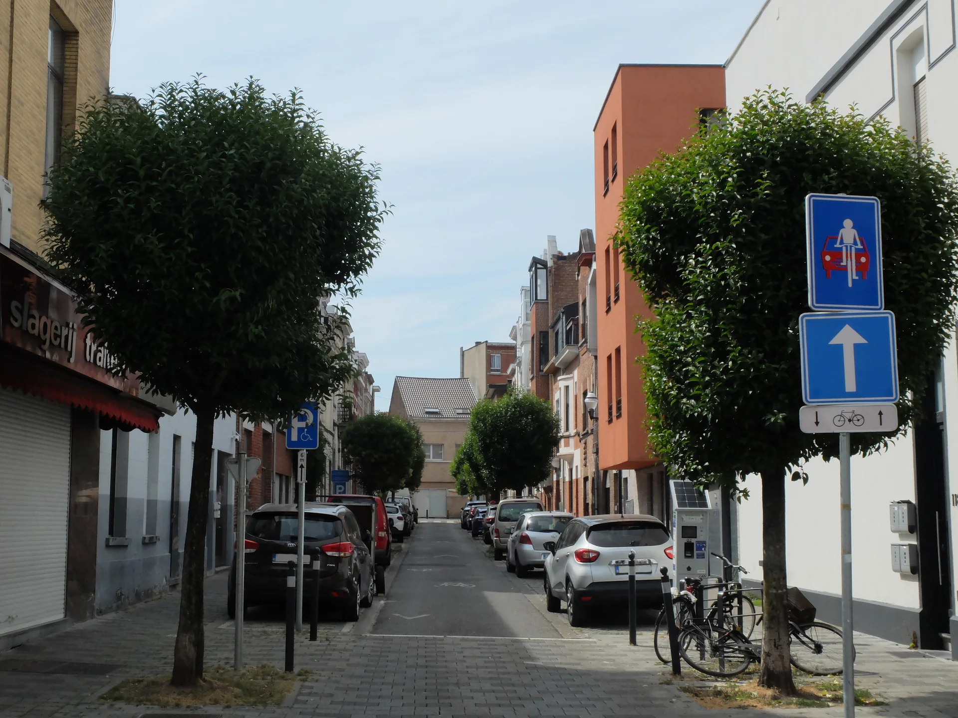 Perspective de la rue Thomaes à Jette, bordée de façades et d’arbres.