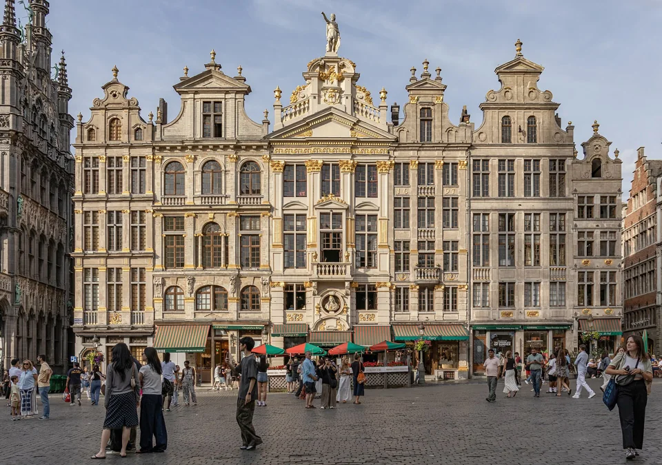 Façades des maisons numérotées de 1 à 7 sur la Grand-Place et passants sur les pavés.