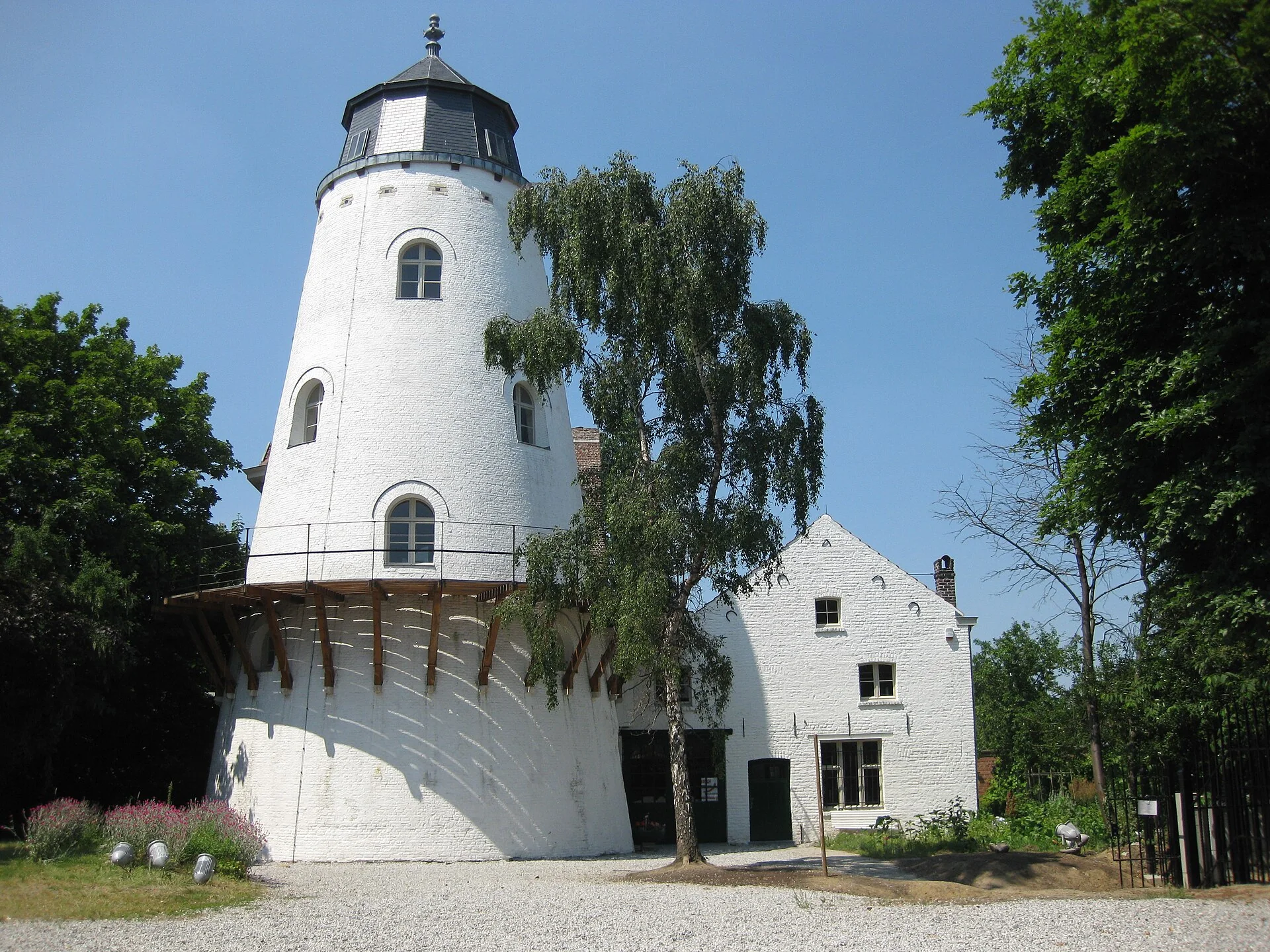 Tour blanche du moulin d’Evere et bâtiment attenant parmi les arbres.