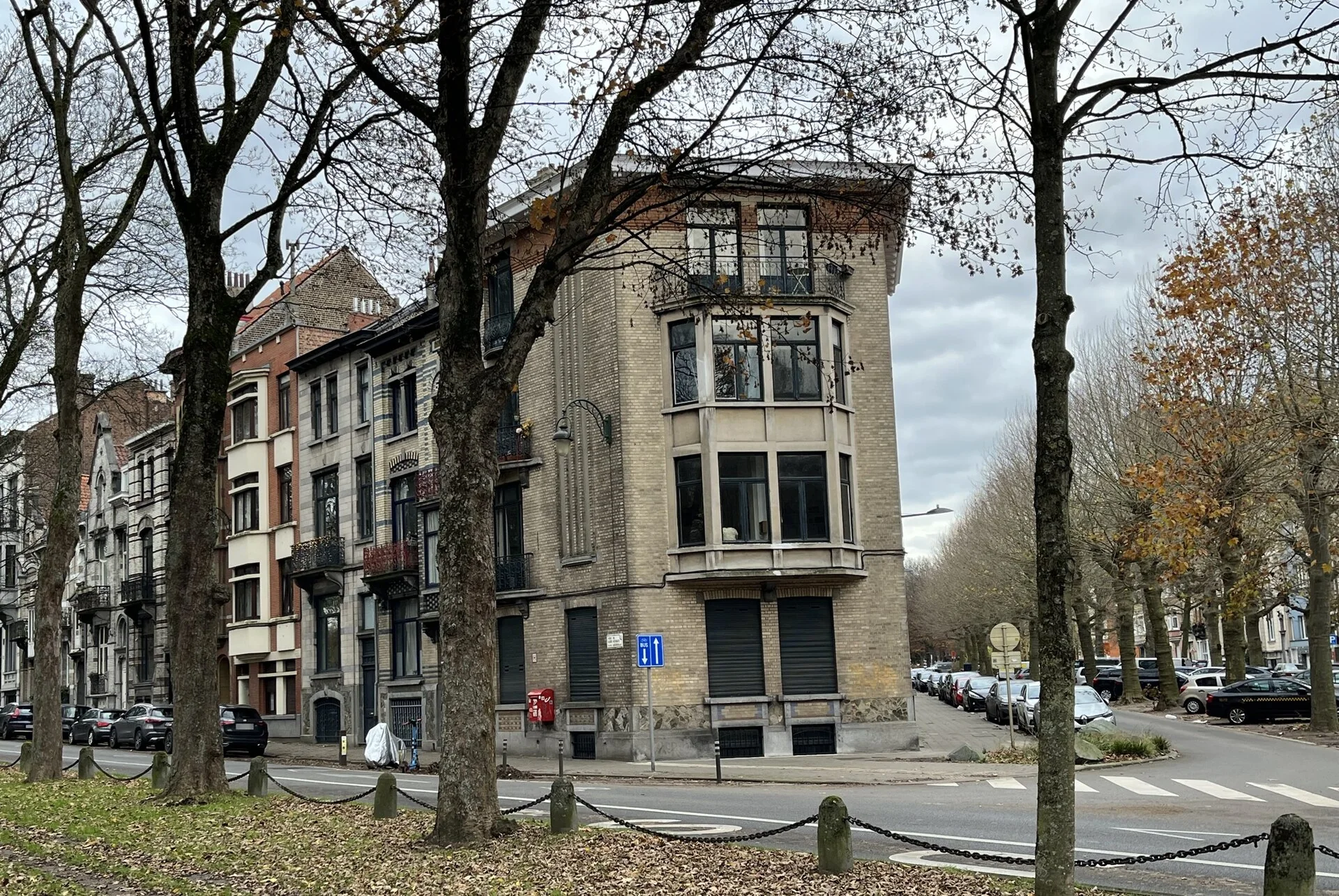 Immeuble d’angle et façades bordées d’arbres au croisement des avenues des Gloires Nationales et de la Constitution.