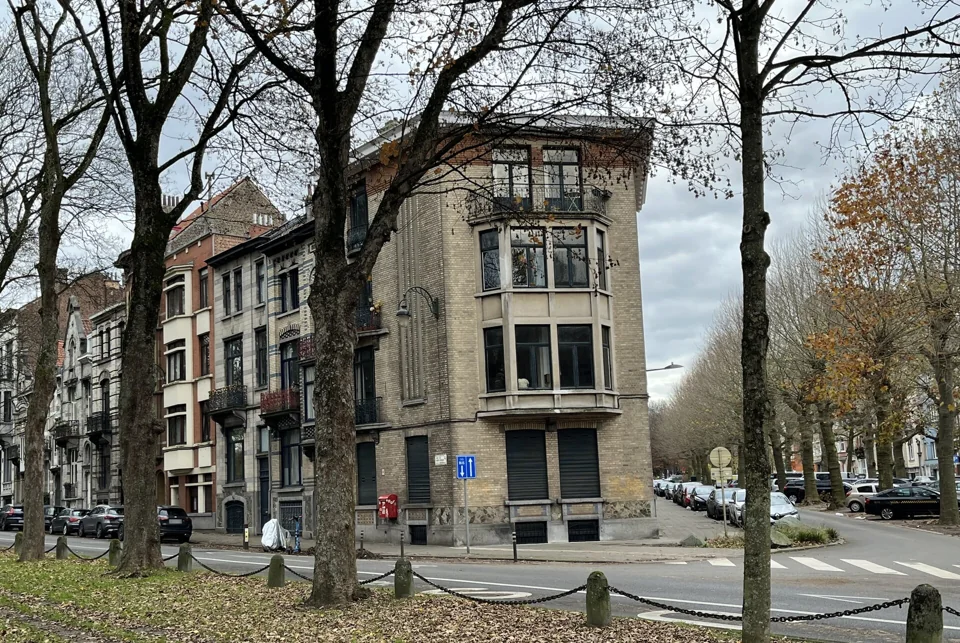 Immeuble d’angle et façades bordées d’arbres au croisement des avenues des Gloires Nationales et de la Constitution.