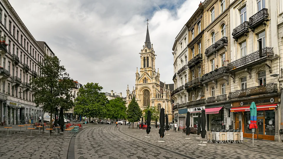 Parvis pavé de Saint-Gilles bordé de façades, avec l’église au bout de la perspective.