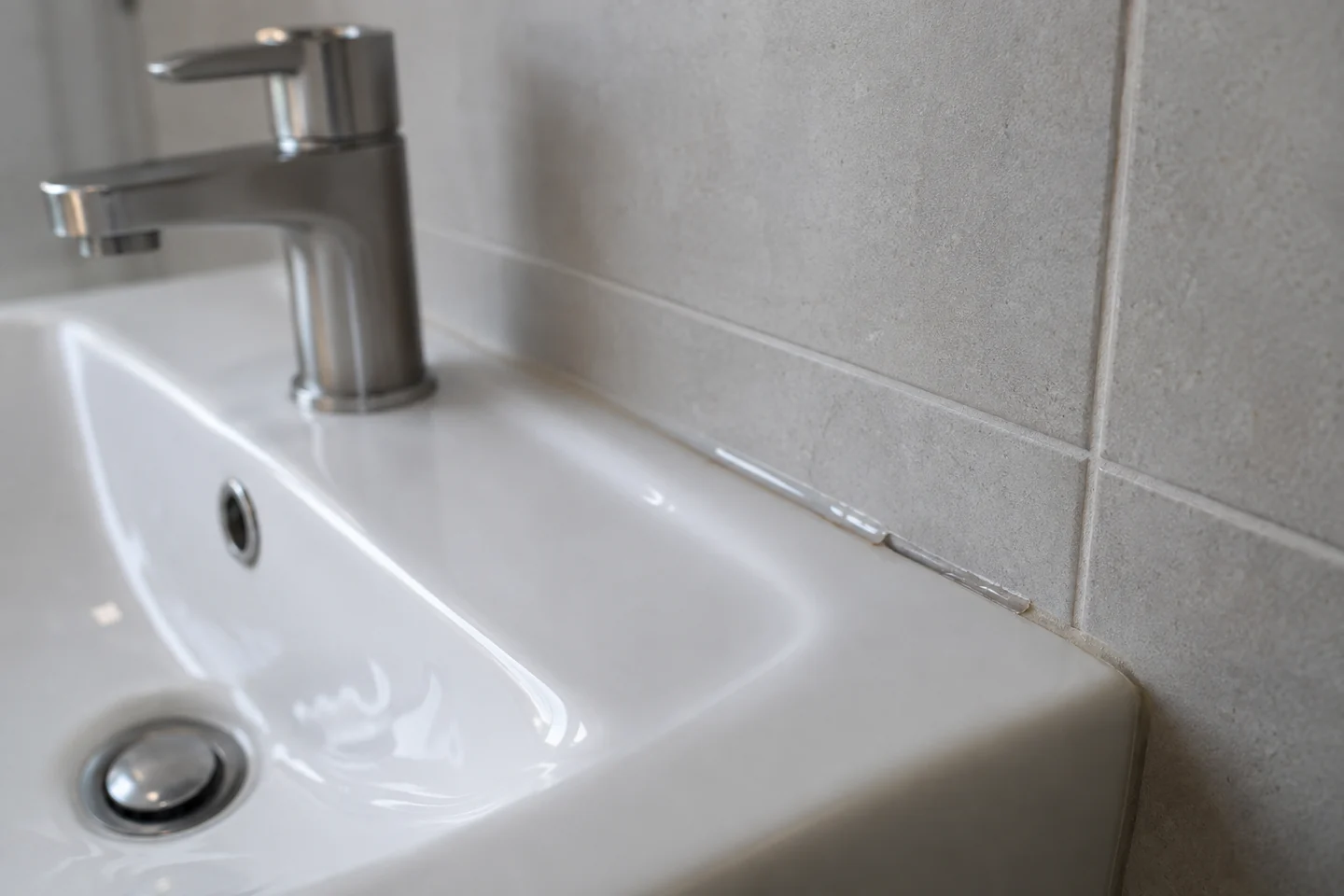 Jonction entre un lavabo et un mur carrelé avec un joint localement incomplet. Illustration.